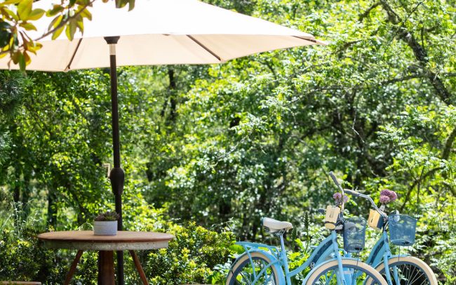 Patio table under an umbrella with two blue bicycles nearby.