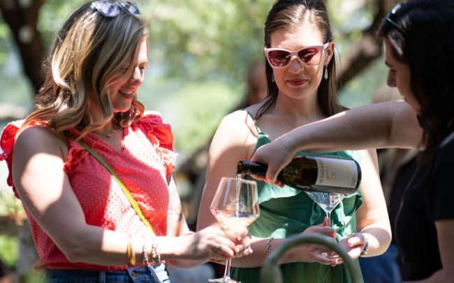 Wine being poured into a glass held by two women outdoors.