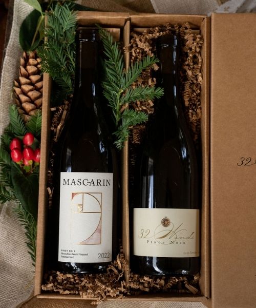 pinotcollection Mascarin and 32 Winds wine bottles in a gift box with pinecones and evergreens.